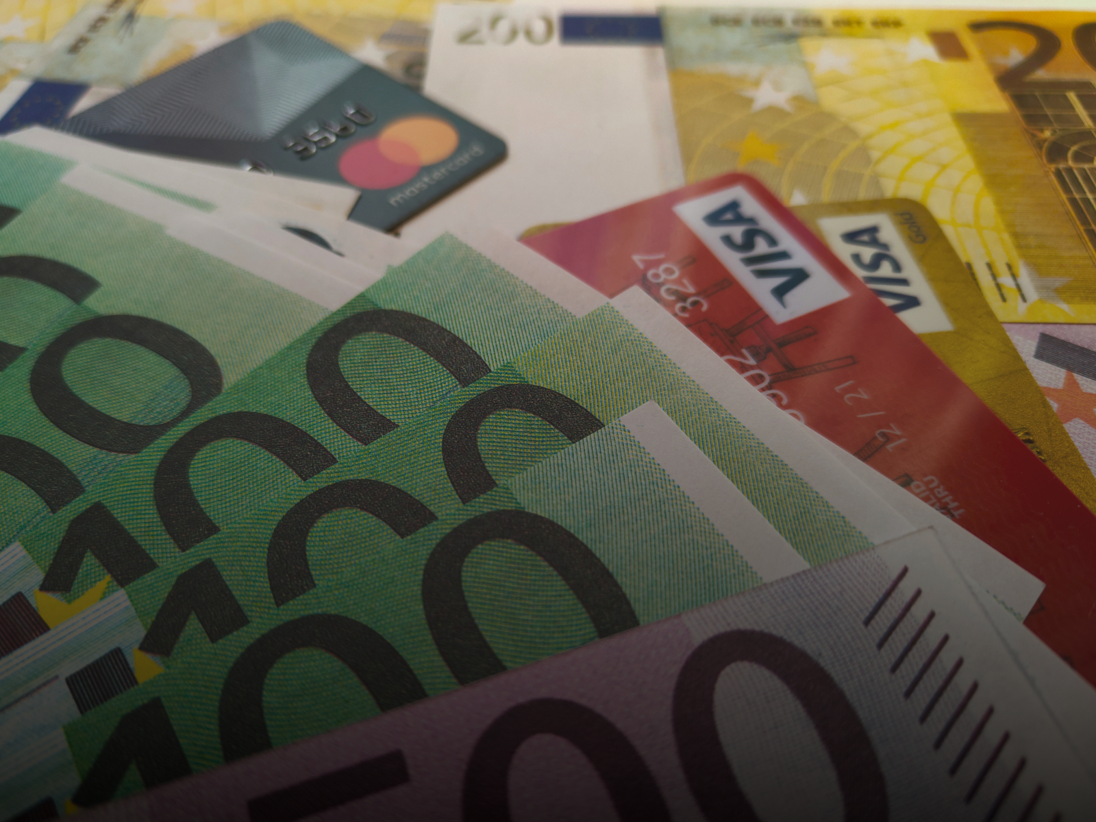 Fanned banknotes with Visa and Mastercard bank cards on top — a visual of cash versus cards in everyday spending