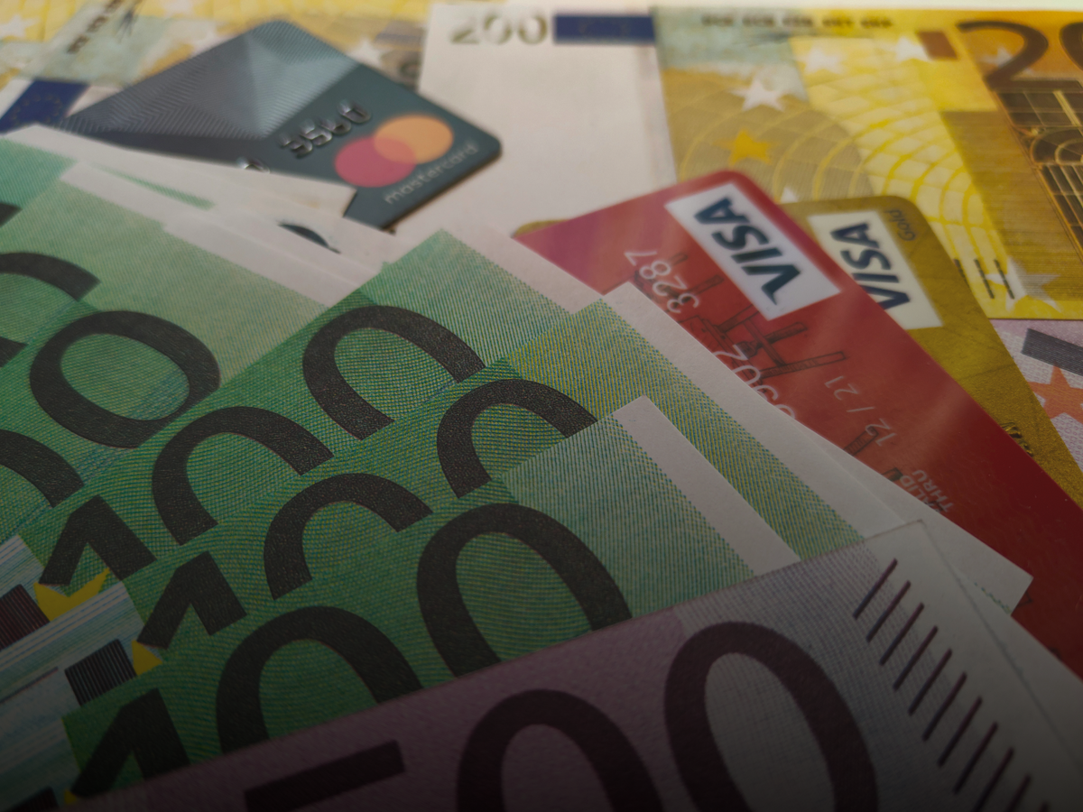 Fanned banknotes with Visa and Mastercard bank cards on top — a visual of cash versus cards in everyday spending