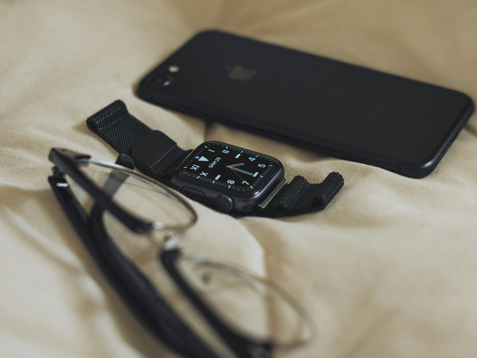 A phone, watch, and glasses laid out on a bed — the minimalist approach to everyday essentials
